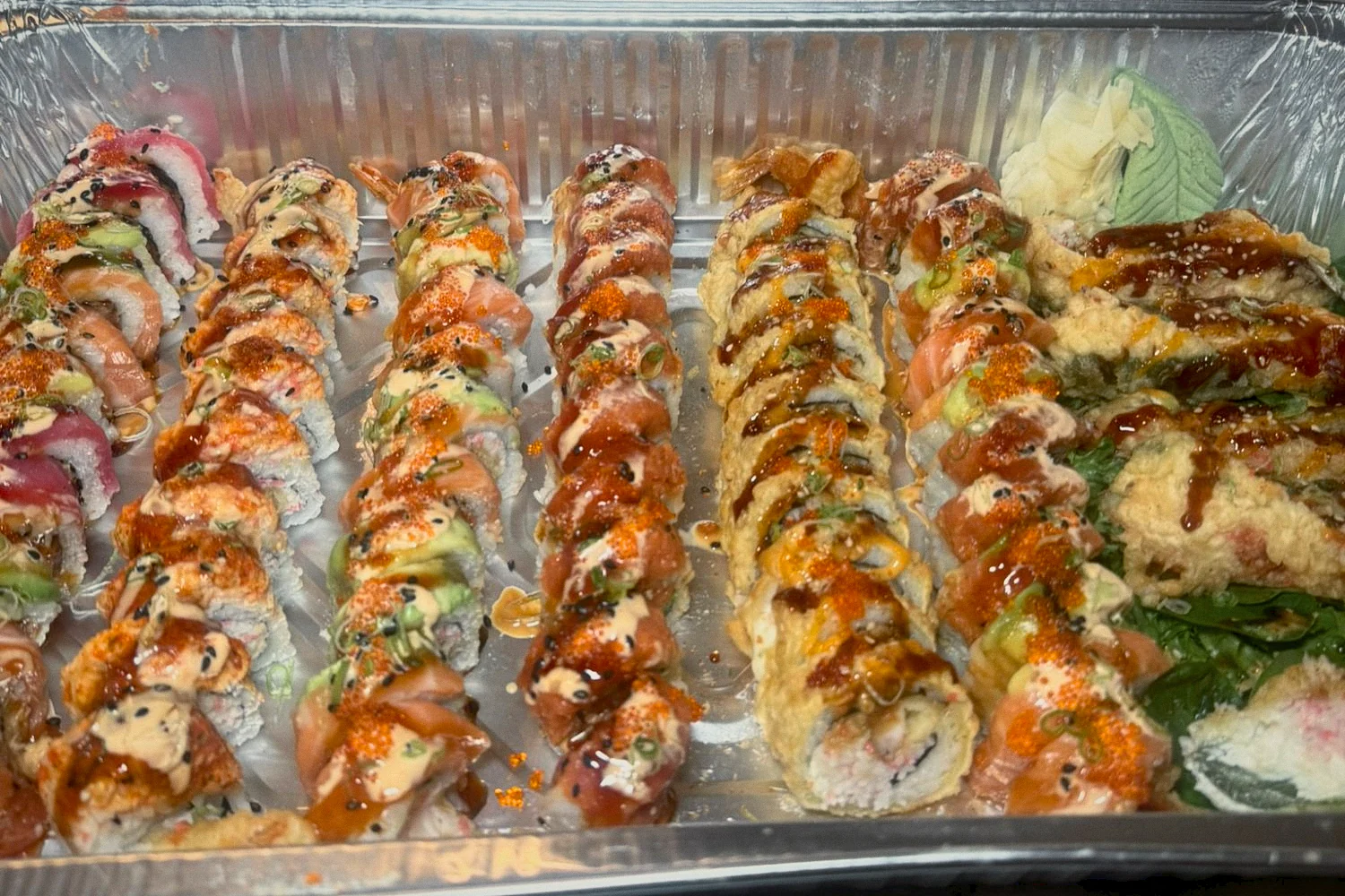 A tray of specialty sushi rolls finished with sauces and tobiko